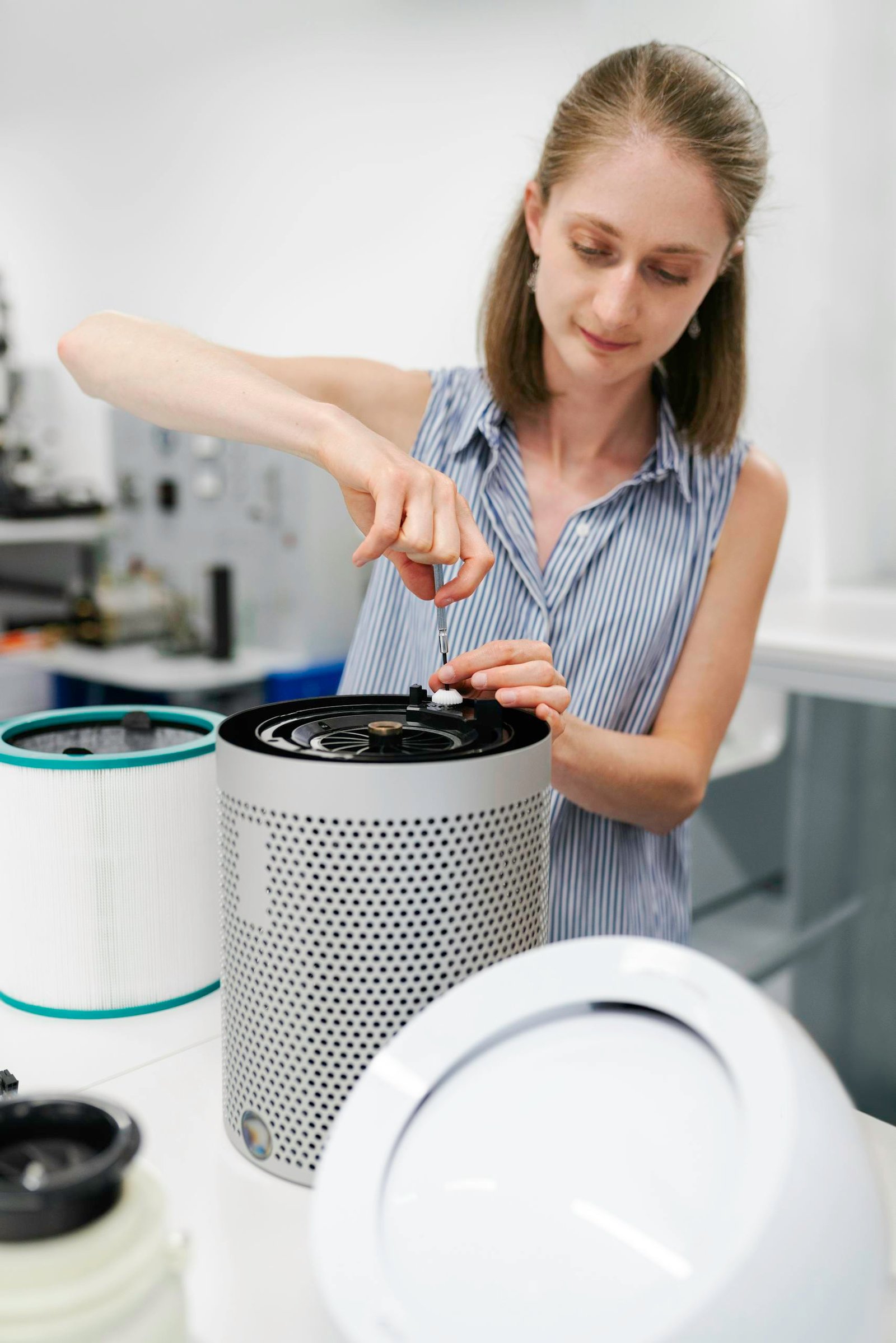 Close-up of a young woman using a screwdriver to repair an air purifier in a laboratory environment.